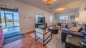 A spacious living room with a television, seating area, and a view of the ocean. - The Bungalow, Pool, Dock, Kayaks, & Game Room (Topping)