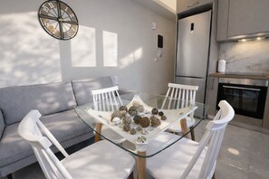 Una cocina moderna con una mesa de comedor de vidrio, sillas blancas y un sofá gris.