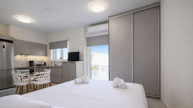 Una habitación de hotel con cama, escritorio, sillas, televisor y vista al cielo.