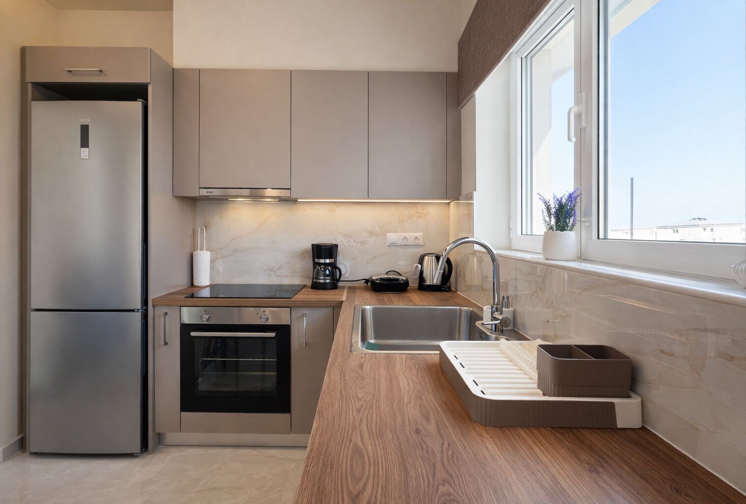 Une cuisine moderne dotée d’appareils électroménagers en acier inoxydable, d’un plan de travail en bois et d’une fenêtre offrant une vue agréable.
