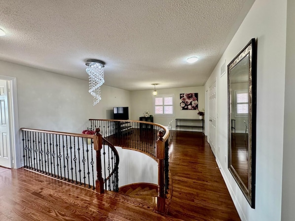 A spacious living area with a wooden staircase, a ceiling light fixture, and a large mirror on the wall.