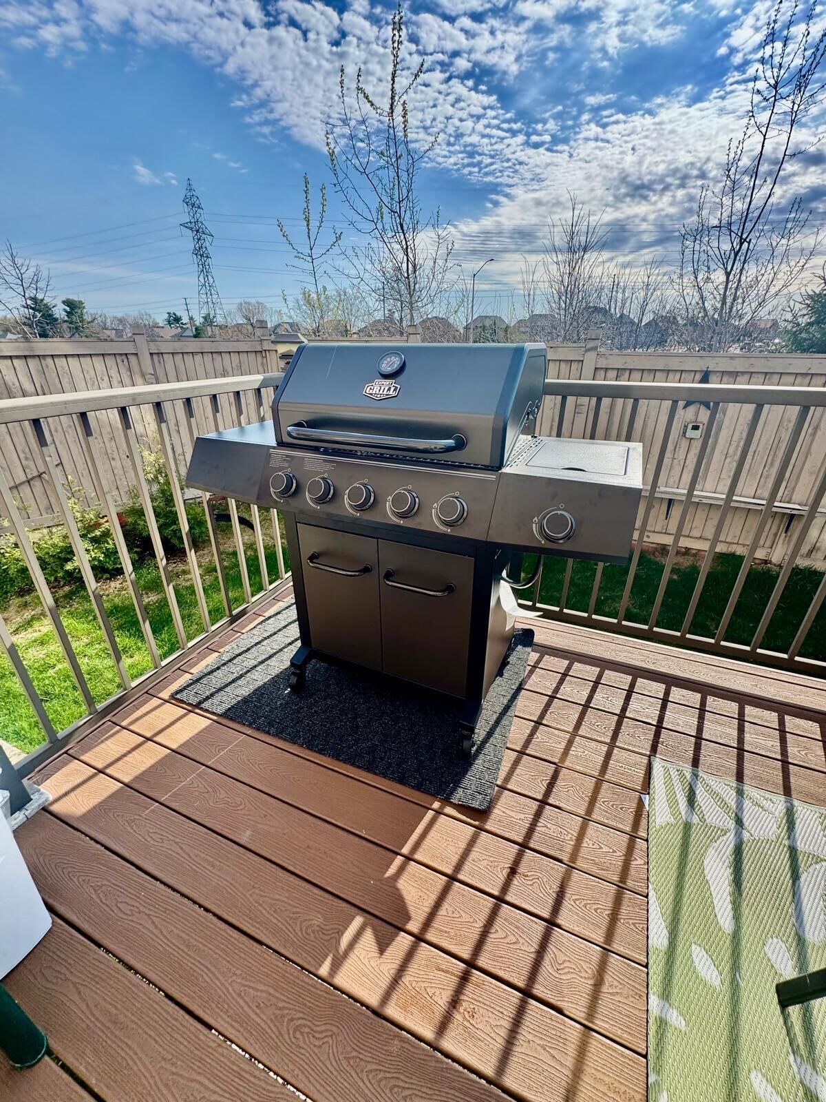 An outdoor grill on a wooden deck with a view of a backyard and a wooden fence.
