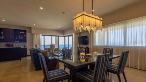Uma sala de estar moderna com área de jantar, uma janela grande com cortinas, uma TV e um candelabro.