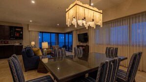 Quarto de hotel moderno com área de refeições, sofá, TV e varanda com vista.