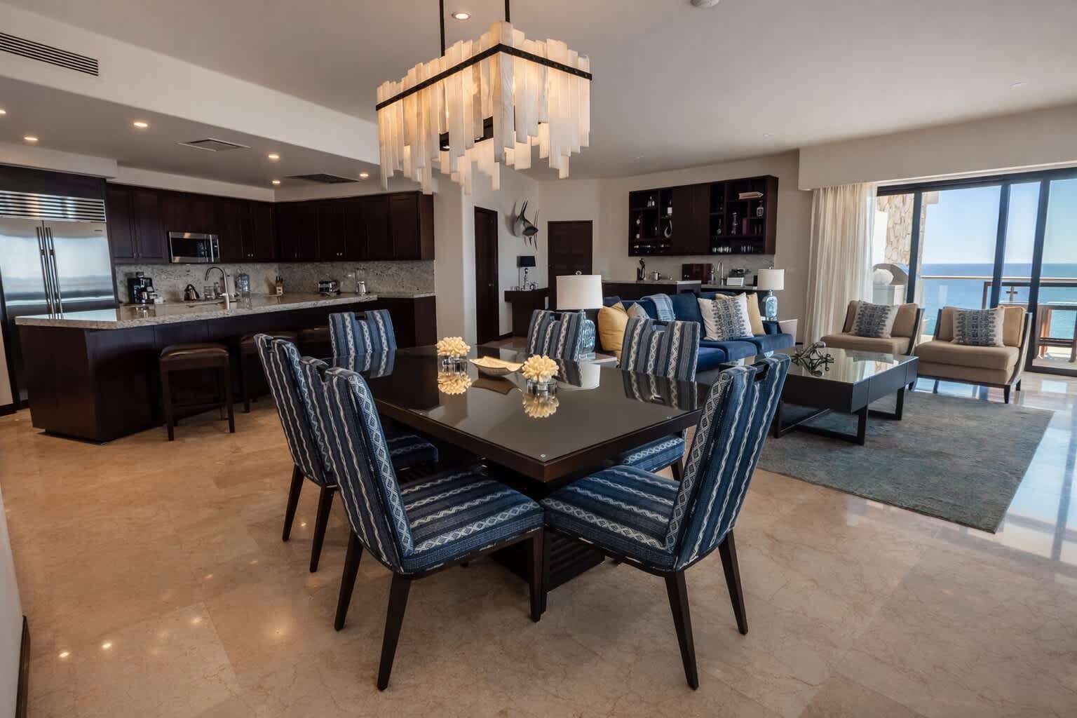 Una cocina moderna con armarios oscuros, una isla central y un comedor con una mesa grande y sillas a rayas azules.