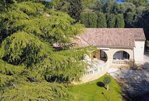 Une villa située sur une colline, avec un toit recouvert de tuiles en terre cuite, une entrée ornée d’une arche en pierre et une végétation luxuriante qui entoure la propriété.