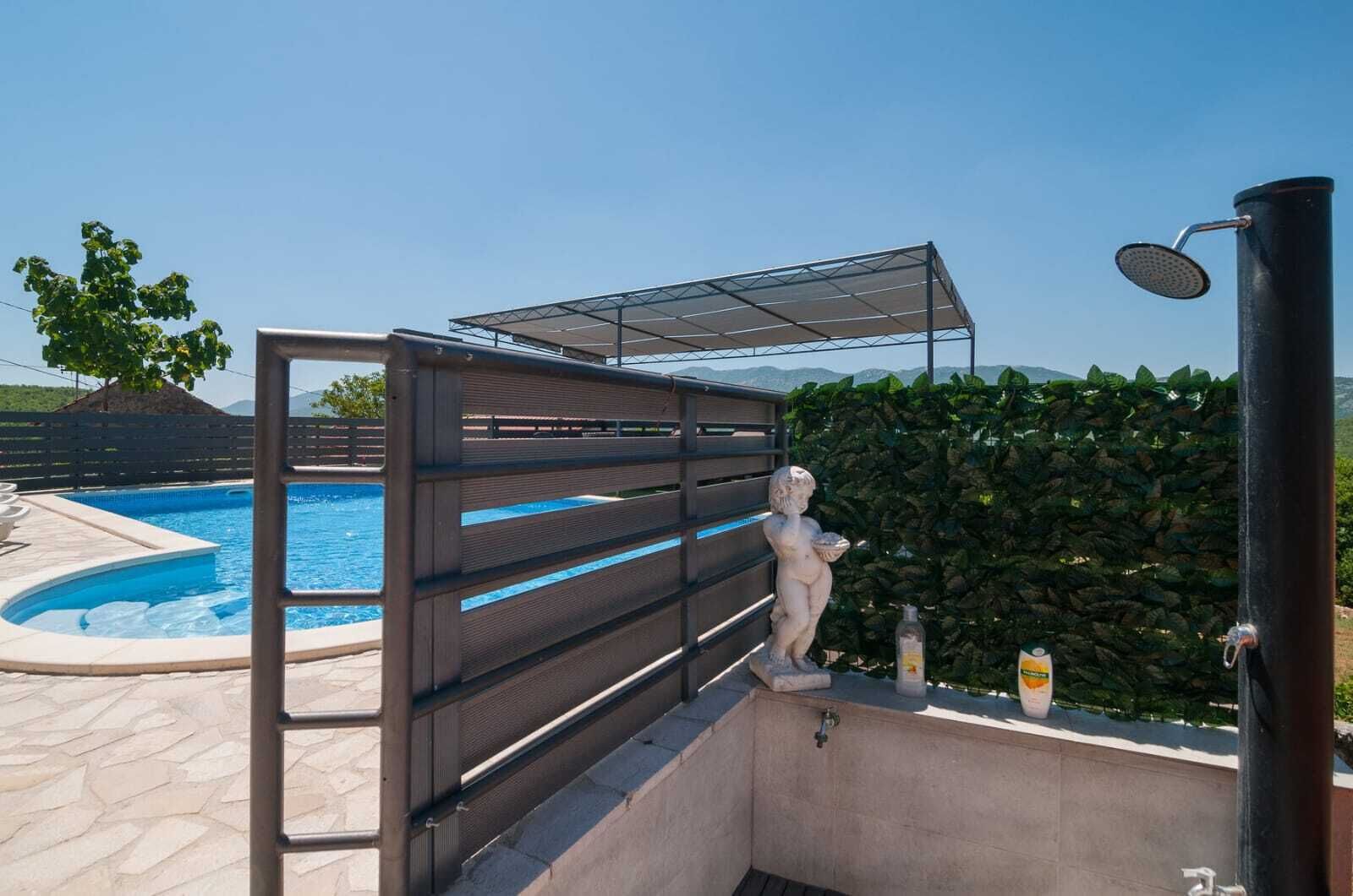 Ein Poolbereich mit überdachter Sitzgelegenheit, einer Statue und einer Dusche.