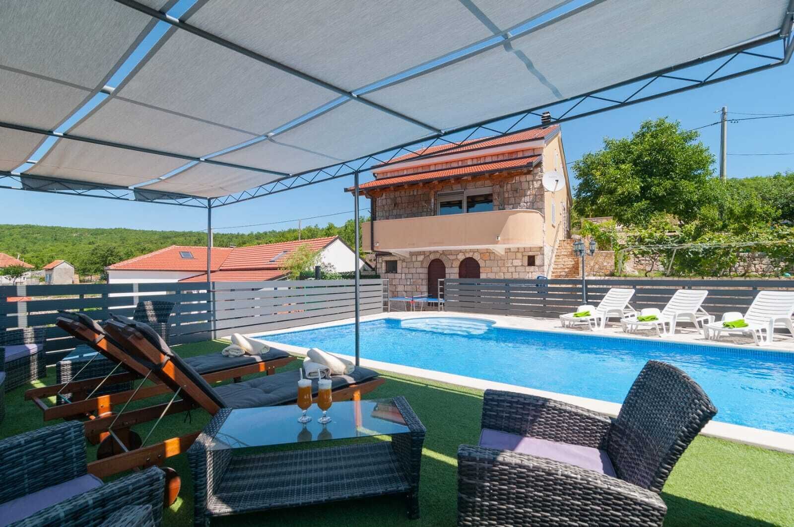 A pool area with lounge chairs, a glass table, and a covered seating area.