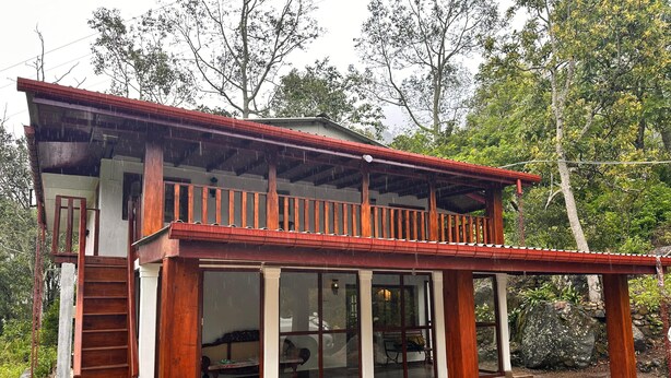 Una casa de madera de dos pisos, con balcón, ventanas grandes y una terraza de madera.