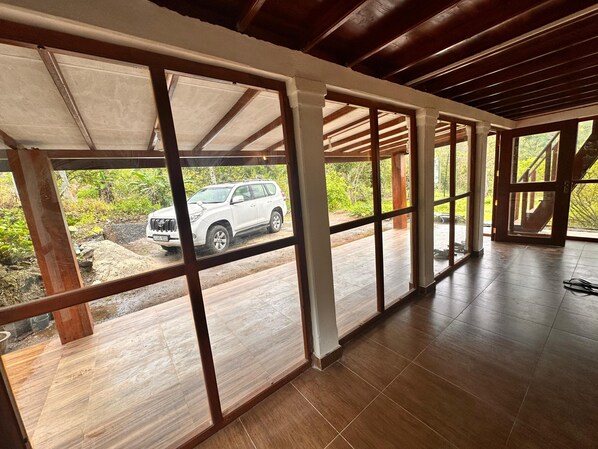 Una habitación amplia con ventanas grandes, suelo de madera y vistas a un SUV blanco en el exterior.