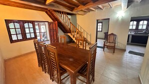 Amplia sala de estar con una mesa y sillas de madera, una escalera y una zona de cocina.