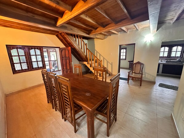 A spacious living area with a wooden dining table and chairs, a staircase, and a kitchen area.