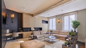 A modern living room with a sofa, ottoman, coffee table, and a TV mounted on the wall. - Superb Duplex in the Center of Paris (Paris)