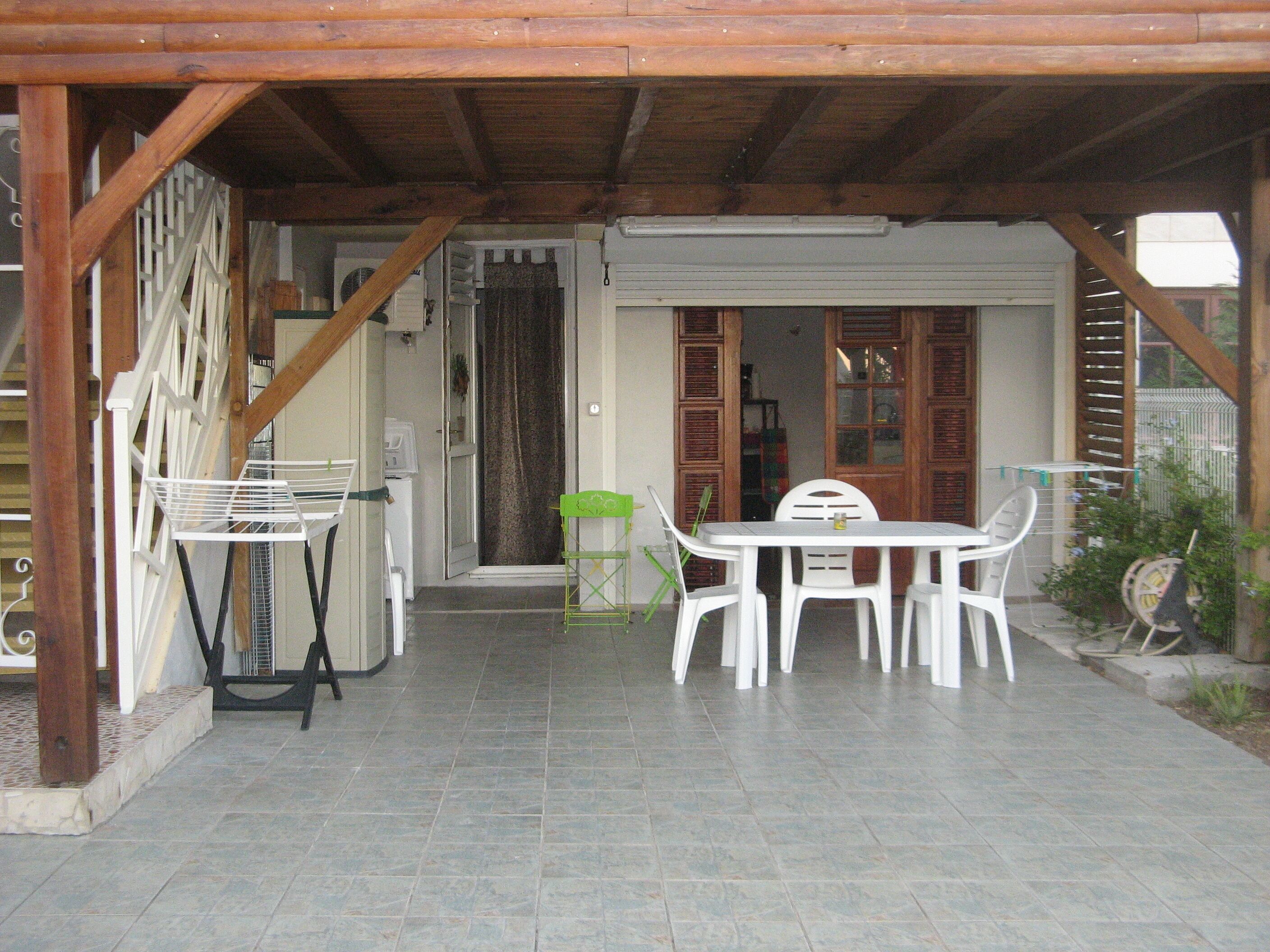 Une terrasse couverte avec une table et des chaises, un étendoir et une porte donnant sur un espace intérieur.