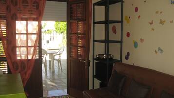 Una habitación con un sofá marrón, una mesita, una silla, un estante y una puerta con cortina.
