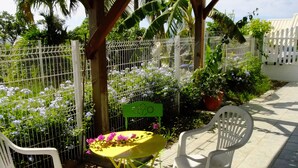Un patio con sillas de plástico blancas, una mesita amarilla y un banco verde.