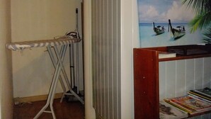 Una habitación con una estantería de madera, un cuadro de una playa y una tabla de planchar.