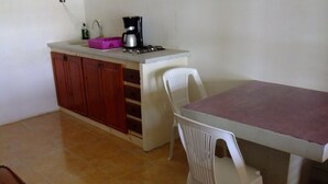 Una cocina pequeña con un lavamanos, una cafetera y un comedor con una mesa y dos sillas.