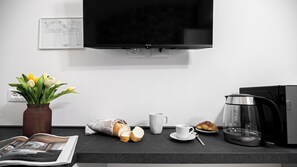 A kitchen counter with a coffee maker, a mug, a croissant, a loaf of bread, and a vase with tulips. - Italianway Easy - The B Village Basic Apt AT02 (Milano)