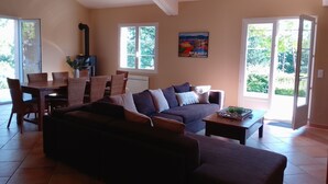 Een woonkamer met een bank, eettafel, stoelen en een open haard.