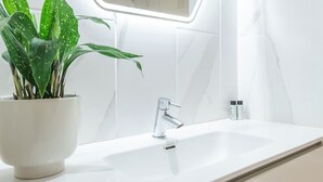 Ein modernes Badezimmer mit einem weißen Waschbecken, einem chromfarbenen Wasserhahn und einer Topfpflanze.