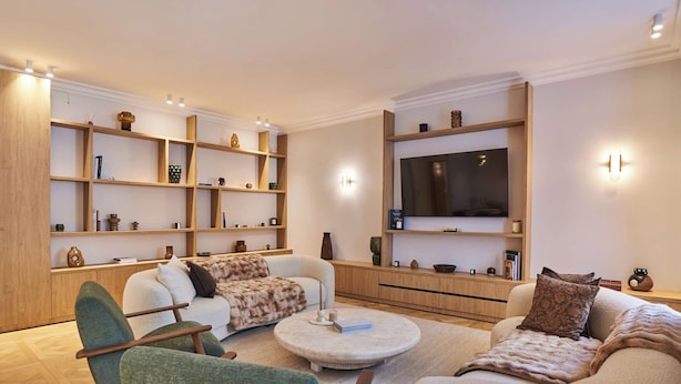 A modern living room with a sofa, armchairs, a coffee table, built-in wooden shelving, and a flat-screen TV. - Luxurious Airconditioned Apartment Arc de Triomphe (Paris)