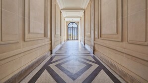 A long hallway with a geometric patterned floor, flanked by beige walls and a central light fixture. - Luxurious Airconditioned Apartment Arc de Triomphe (Paris)