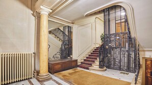 A grand staircase with ornate metal railings, a marble floor, and a wooden bench. - Luxurious Airconditioned Apartment Arc de Triomphe (Paris)