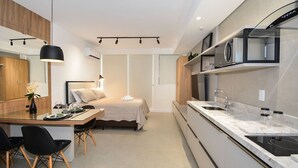 A modern kitchen with a microwave, stove, and sink. There is a dining area with a table and chairs. - Studio em frente a UFSC e HU - 309A (Florianópolis)