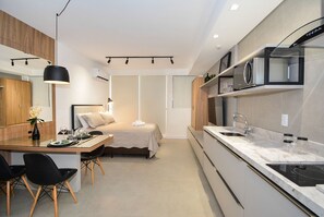A modern kitchen with a microwave, stove, and sink. There is a dining area with a table and chairs. - Studio em frente a UFSC e HU - 309A (Florianópolis)