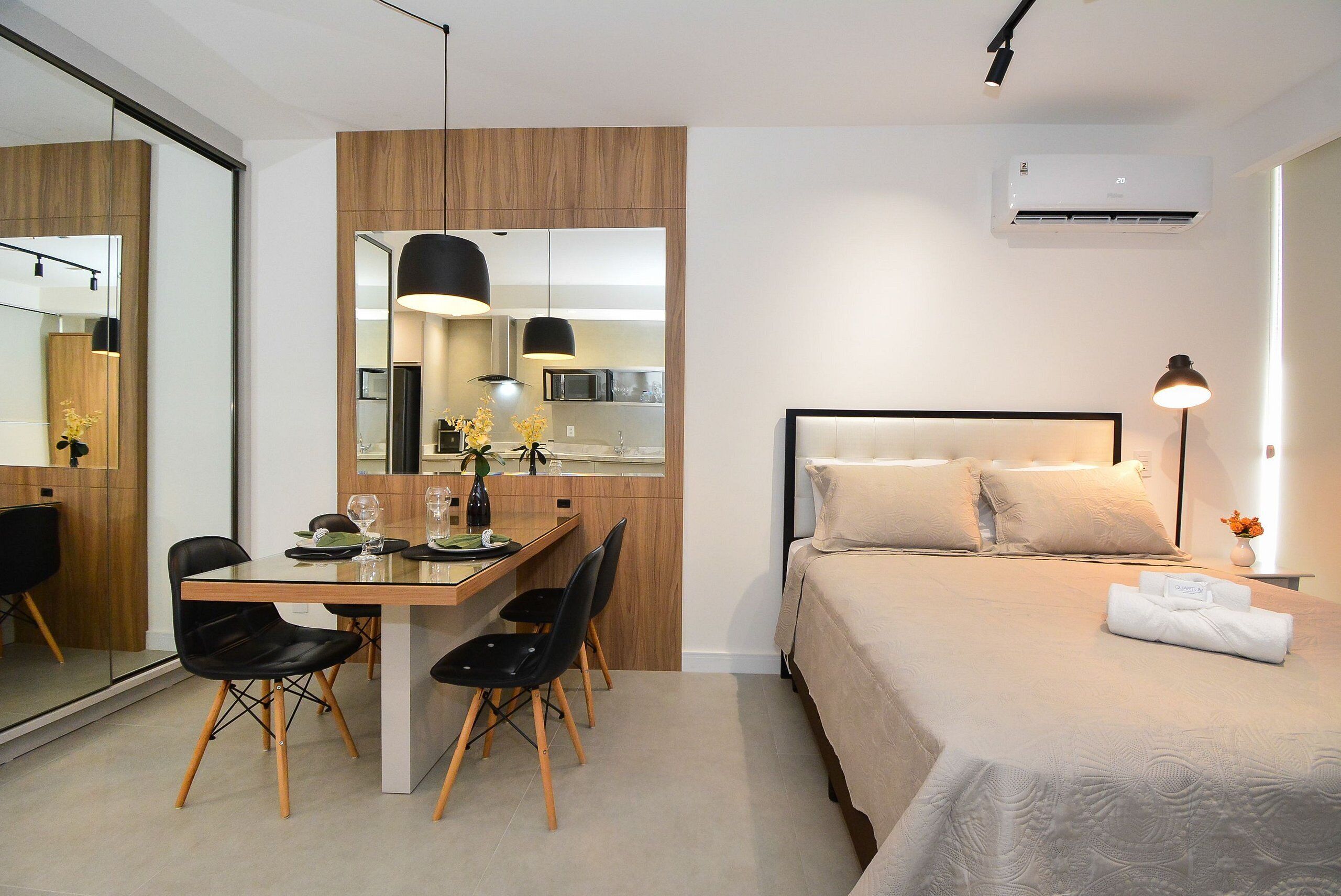 A modern hotel room with a bed, bedside table, and a dining area with chairs and a table.