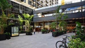 Et bytorv med moderne bygninger, udendørs siddepladser og grønne områder.