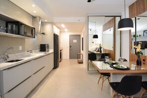 A modern kitchen with a built-in microwave, a coffee machine, and a dining area with a table set for two. - Studio em frente a UFSC e HU - 309A (Florianópolis)