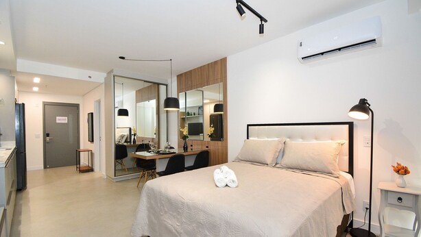 A modern hotel room with a large bed, a desk, a mirror, and an air conditioning unit. - Studio em frente a UFSC e HU - 309A (Florianópolis)