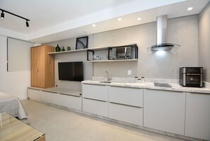 A modern kitchen with built-in appliances, a flat-screen TV, and a minimalist design. - Studio em frente a UFSC e HU - 309A (Florianópolis)
