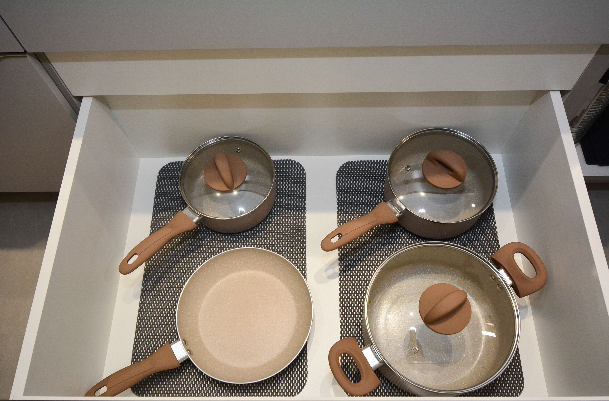 A kitchen drawer with three pots and pans, each with a brown handle, and a spatula.