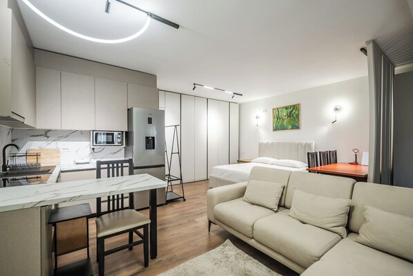 A modern, compact living space with a kitchenette, a dining area, a sofa, and a bed.