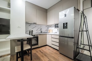 A compact kitchen with a built-in oven, a microwave, and a stainless steel refrigerator.