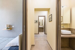 Un couloir étroit mène à une salle de bain équipée d’un lavabo et d’un miroir.