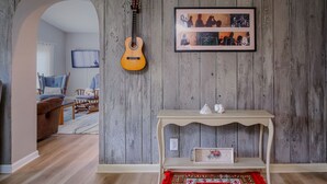 Ein Zimmer mit einer Holzwand, einer Gitarre, einem gerahmten Bild, einem kleinen Tisch mit Dekoration und einem gemusterten Teppich.