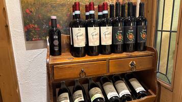Un porte-bouteilles en bois contenant plusieurs bouteilles de vin, dont des variétés « Feus » et « Syrah », est adossé à un mur texturé sur lequel est accrochée une peinture.