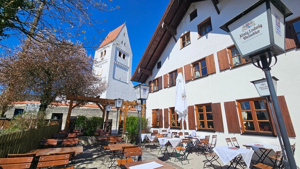 An outdoor seating area with tables and chairs, a white building with wooden shutters, and a bell tower. - Room 11 Standard Double Room with Wi-Fi (Seefeld)