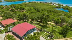 A large house with a red roof, surrounded by lush greenery and a clear view of the ocean. - Infinity Pool & Ocean View Studio - Sunset (Santos Guardiola)