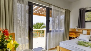 A bedroom with a bed, a table with a vase of flowers, and a view of the outdoors. - Infinity Pool & Ocean View Studio - Sunset (Santos Guardiola)