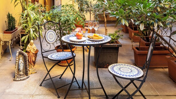 Un cortile con un tavolo rotondo, due sedie, piante in vaso e una statua.
