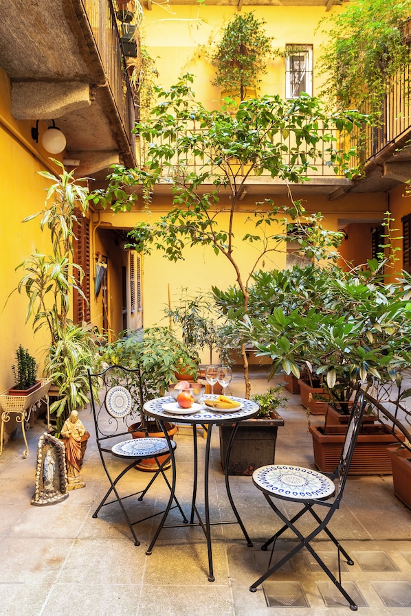 A courtyard with a round table, two chairs, potted plants, and a statue. - Apartment Porta Ticinese - Navigli (Milano)