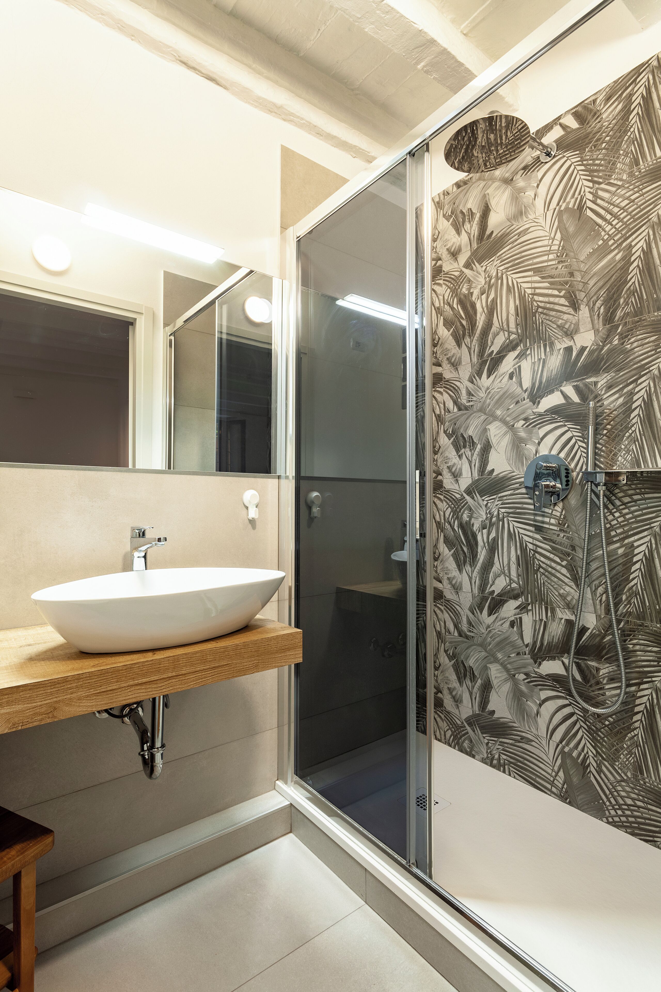 Ein Badezimmer mit einem weißen Waschbecken, einem Spiegel und einer Dusche mit einer Wand mit Blattmuster.