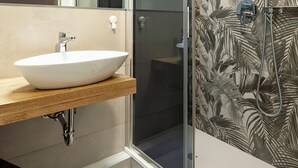 Un bagno con un lavandino bianco, uno specchio e una doccia con decorazioni a motivo di foglie.