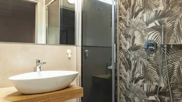 Ein Badezimmer mit einem weißen Waschbecken, einem Spiegel und einer Dusche mit einer Wand mit Blattmuster.