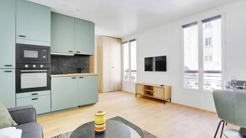 Een moderne keuken met inbouwapparatuur, een eethoek met een tafel en stoelen, en een aan de muur bevestigde televisie.